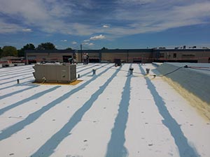 Roof-Restoration-Kentwood-MI-Michigan-1 | JM Roofing Solutions Flat roof with white reflective membrane, blue seams, and an HVAC unit on the left, distant industrial buildings under a blue sky.