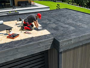 Flat-Roof-Repair-Wyoming-MI-Michigan-2 | JM Roofing Solutions Construction worker kneeling on a flat roof, applying roofing membrane with tools nearby on the decked surface.