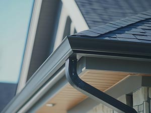 Gutter-Installation-Wyoming-MI-Michigan-2 | JM Roofing Solutions Close-up of a black gutter and roofline on a modern house, showing the downspout and eaves.